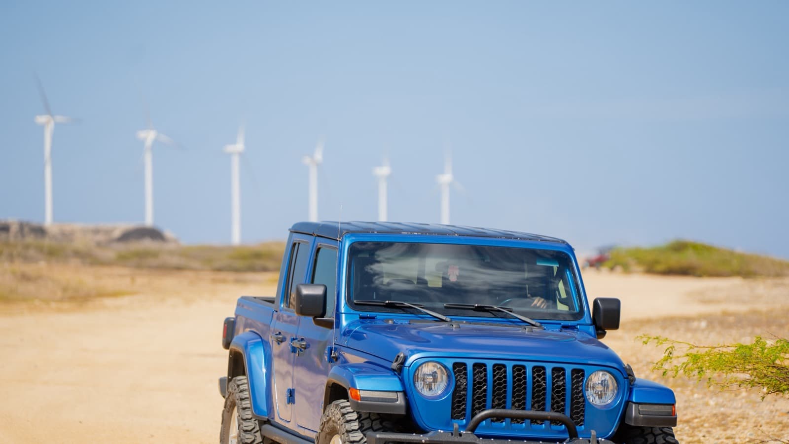 A blue Jeep Gladiator on a dirt road with Aruba's wind turbines in the background