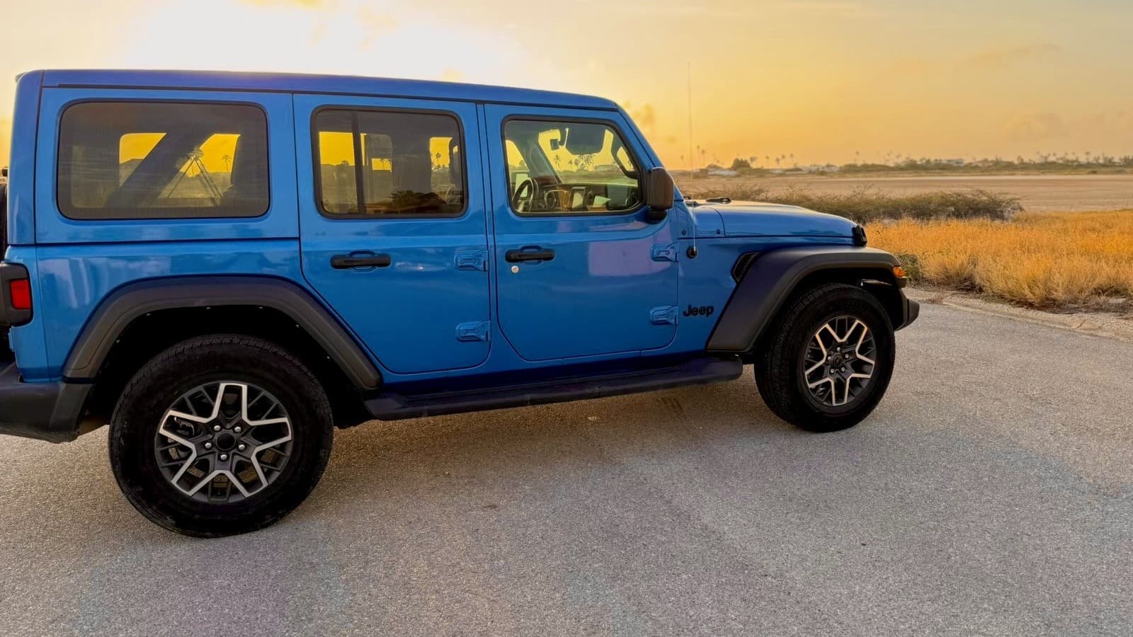 A blue Jeep Wrangler parked on a road at sunset in Aruba