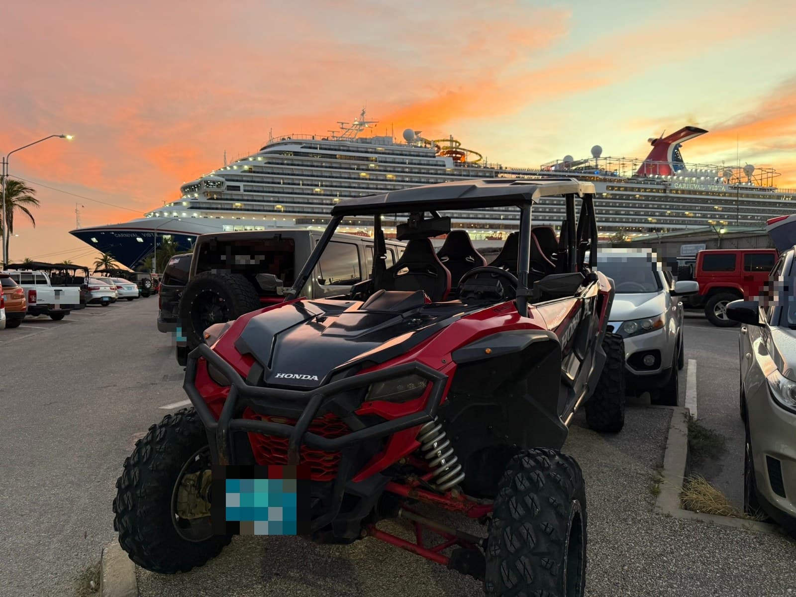 A red Honda UTV parked in the port car park with a cruise ship docked behind it at sunset