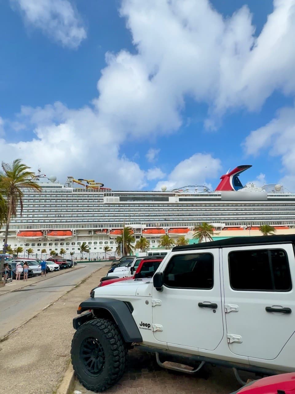 A white Jeep Gladiator parked at the Aruba cruise terminal with a cruise ship docked behind it