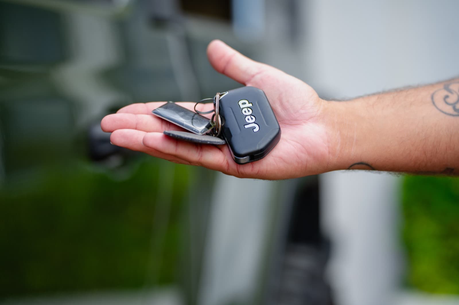 A hand holding out a Jeep key fob outdoors at Aruba airport pickup