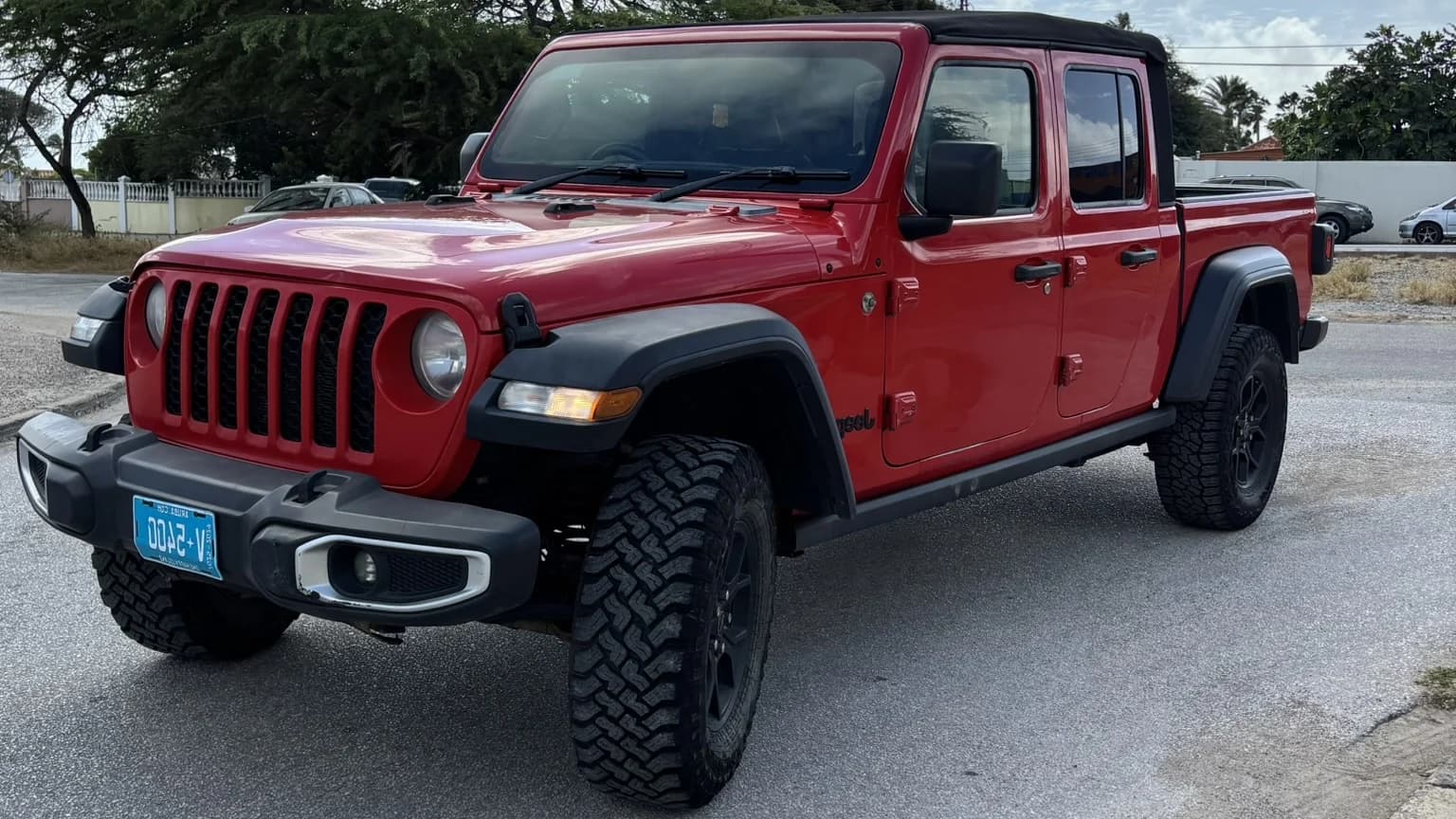 A red Jeep Gladiator parked on a paved street in Aruba, seen from the front three-quarter