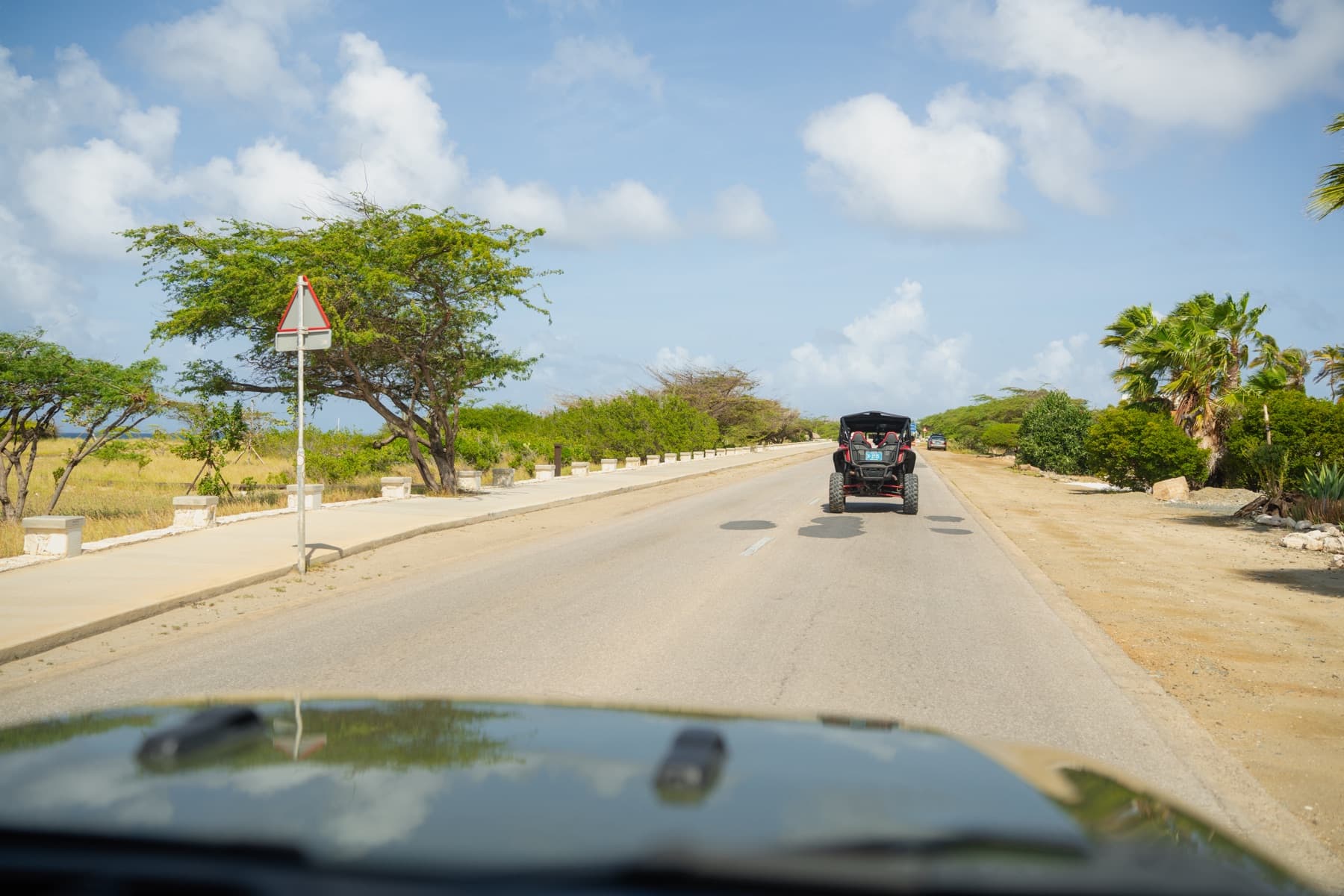 A paved Aruba road seen from the driver's seat, with a Jeep ahead