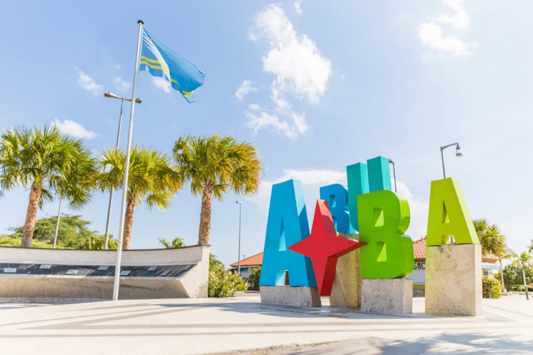 The colourful Aruba sign beside the Aruban flag, with palm trees behind